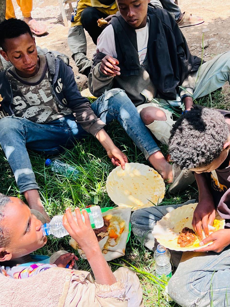 Group of children sitting on the grass sharing a meal