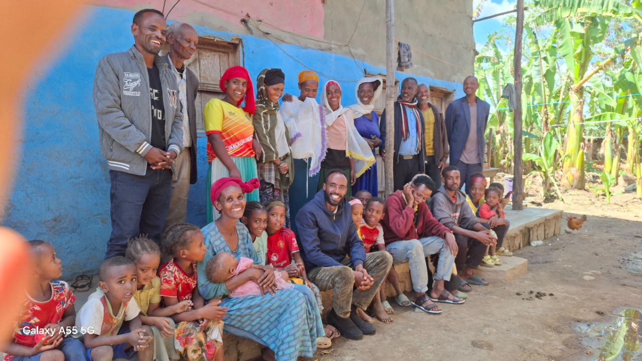 Large group photo of a family and community members outside their home