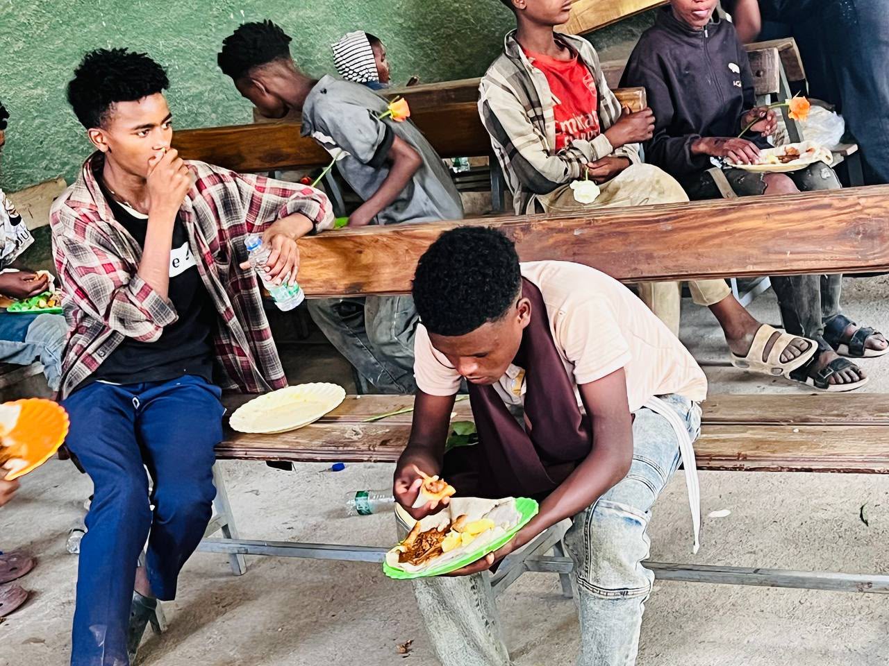 Young men sitting on benches eating a meal