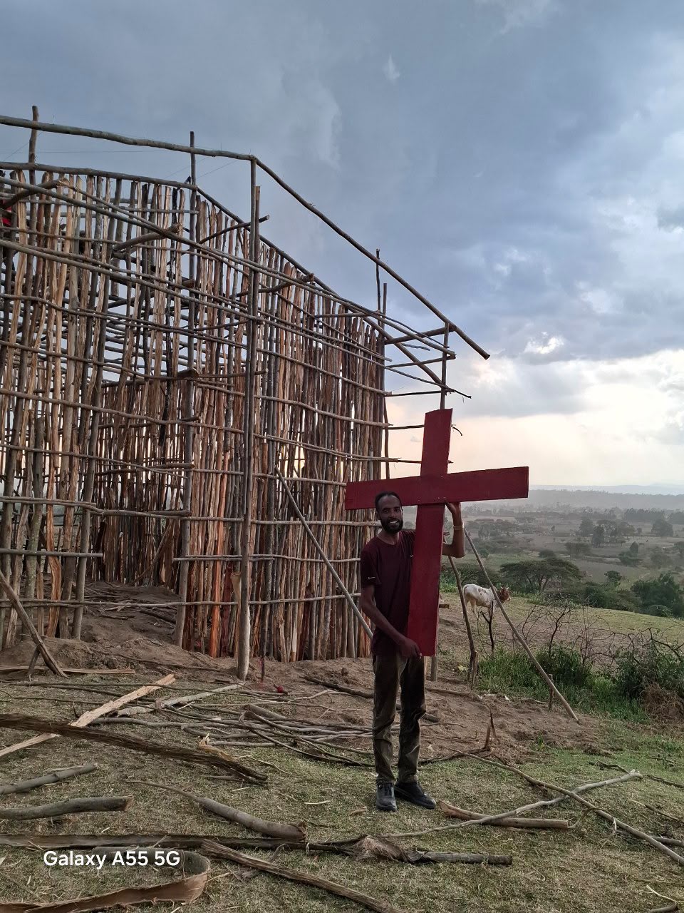 Man carrying the wooden cross beside the church frame at dusk