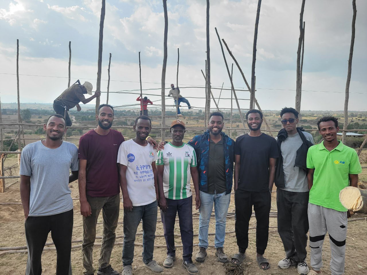 Group of volunteers posing in front of the church frame while workers tie the roof poles