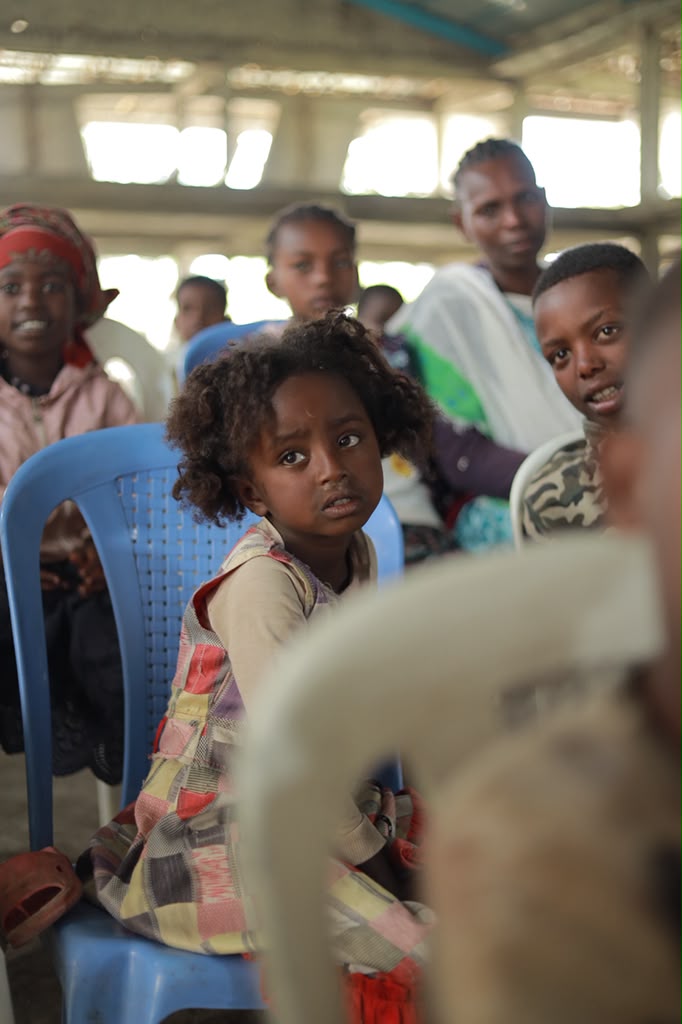 Young girl sitting on a chair among a crowd at an indoor event