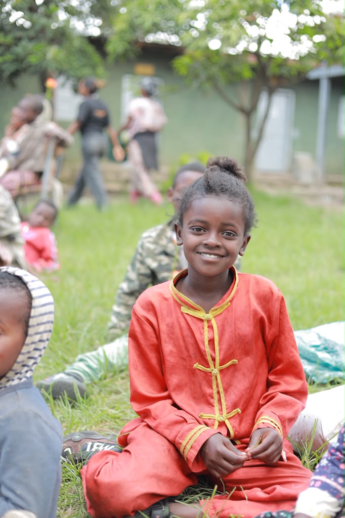 Girl in a red traditional outfit smiling outdoors at an outreach event